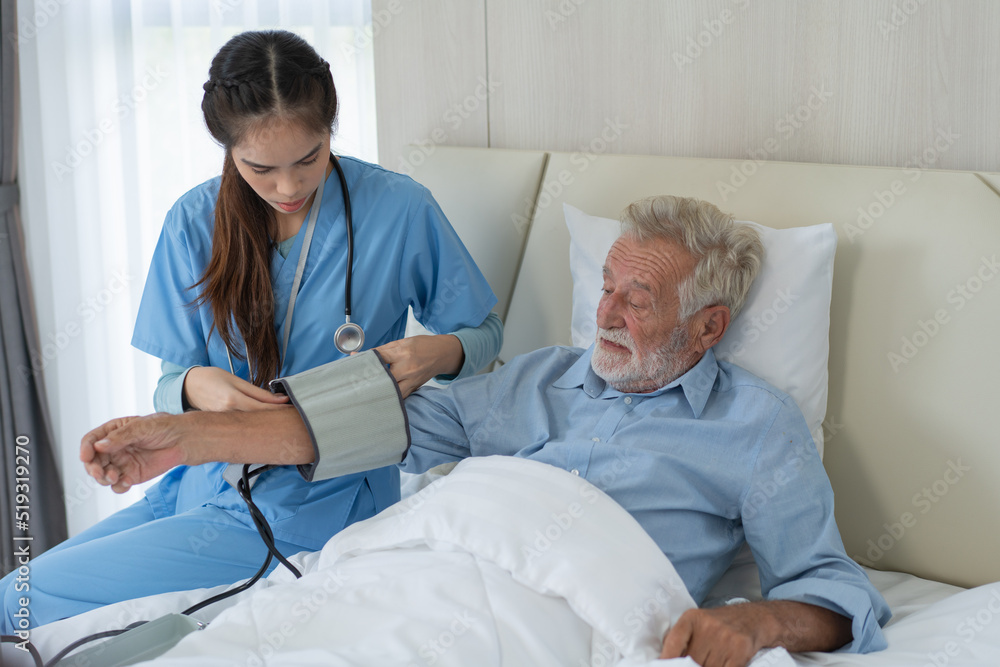 Obraz premium Asian nurse caregiver equip blood pressure gauge to senior patient resting on bed. Female therapist take care of grandfather recovery in nursing home. healthcare and medical insurance
