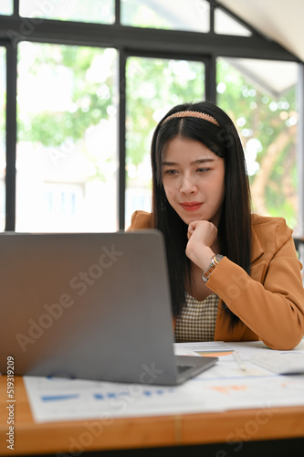 Beautiful Asian businesswoman focused working on her task, using laptop in the office.