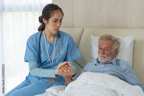 Asian female caregiver holding senior man hand giving support and empathy. woman taking care of patient on bed in nursing home. healthcare and medical insurance concept