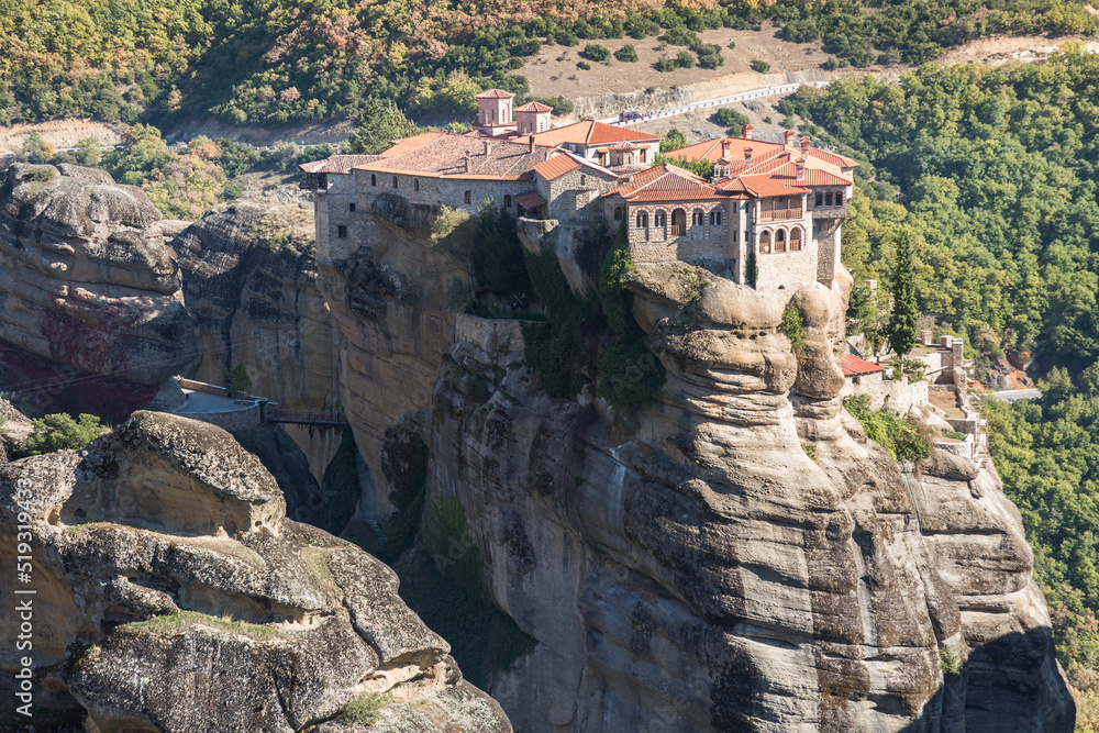 Naklejka premium Beautiful scenic view, Orthodox Monastery of Varlaam, immense monolithic pillar, green foliage at the background of stone wall in Meteora, Pindos Mountains, Thessaly, Greece, Europe