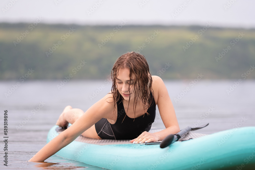 Fototapeta premium A beautiful girl is floating on a supboard on a river. Young woman supsurfing at sunrise.