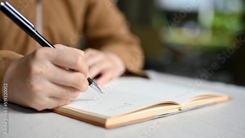 A female college student writing her homework on a school notebook. Close-up and focus hand