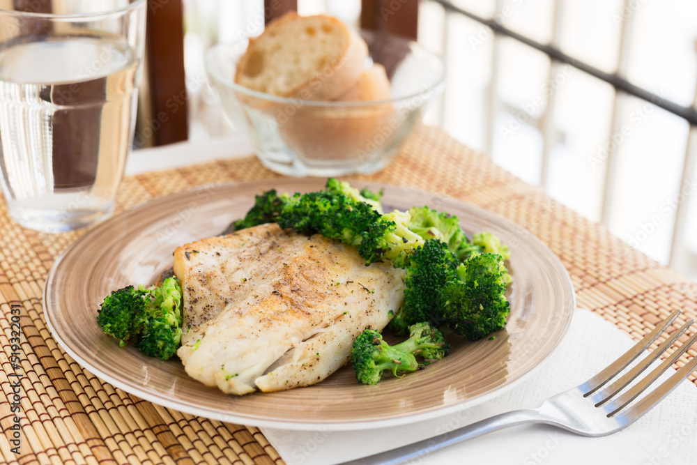 fried fillet of sea bass with garnish of broccoli on black warm stone plate fried fillet of sea bass with garnish of broccoli on black warm stone plate