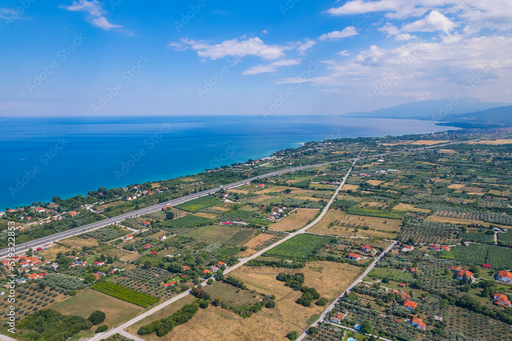 Aerial view of calm Aegan Sea and seashore. Greek houses with orange roofs among gardens, forests, and farmlands. High quality photo