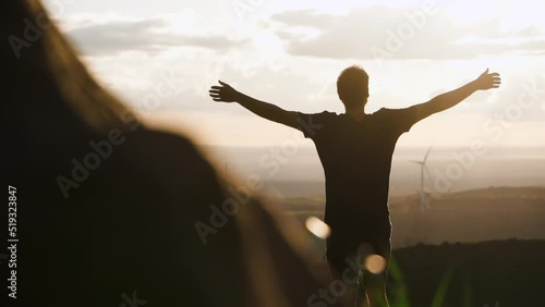 young male celebrating life with open arms in scenic sunset hill with windmill farm at distance, happiness eco sustainable travel green concept photo