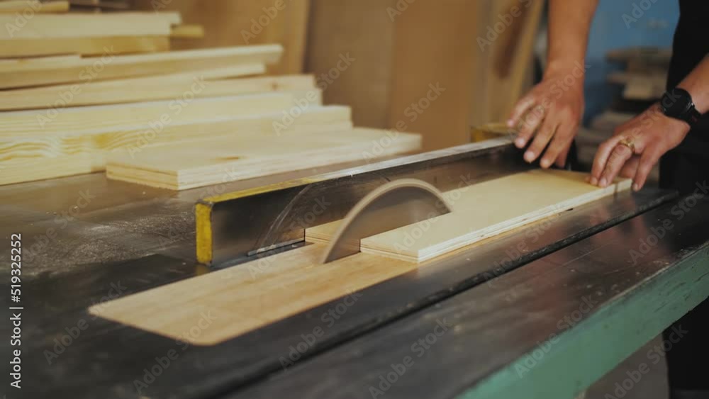 A running blade on a bench saw sawing trough the wooden log in the middle of a working space, close up footage. A sawing circle that cuts the board, slow motion shot. A running blade on a bench saw sawing trough the wooden log in the middle of a working space, close up footage. A sawing circle that cuts the board, slow motion shot.