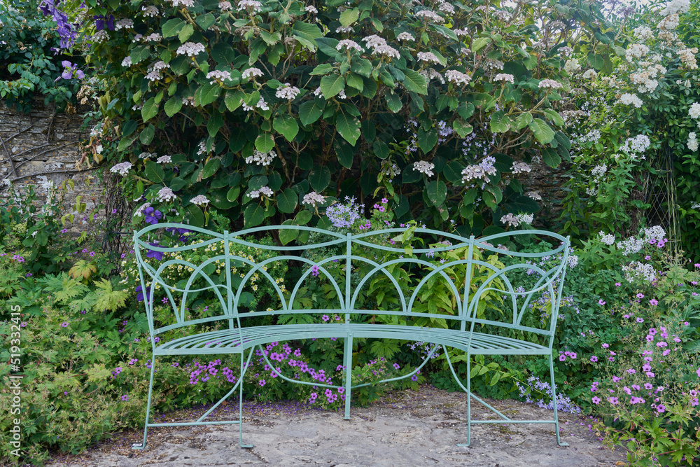 Ornate green metal garden bench surrouned by flowers Ornate green metal garden bench surrouned by flowers