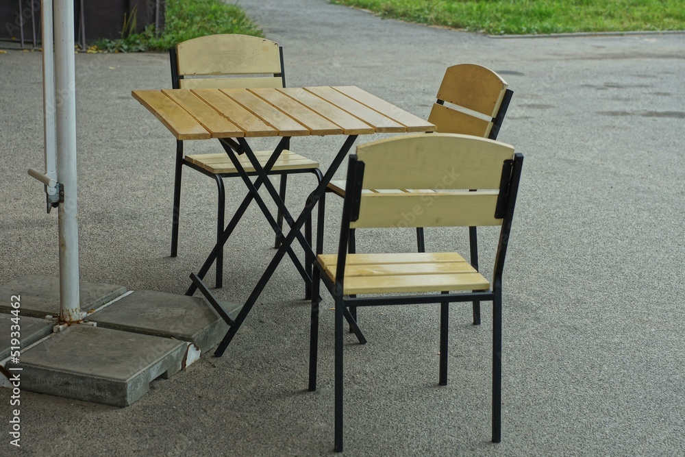 three iron beautiful comfortable with a beige wooden base black chairs and a table stand outside during the day