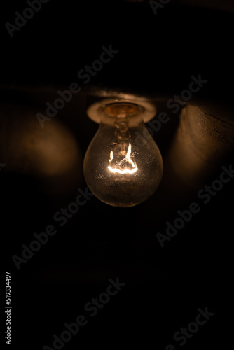 Very dim incandescent light bulb mounted on a cellar ceiling. Close up shot, no people, glowing filament