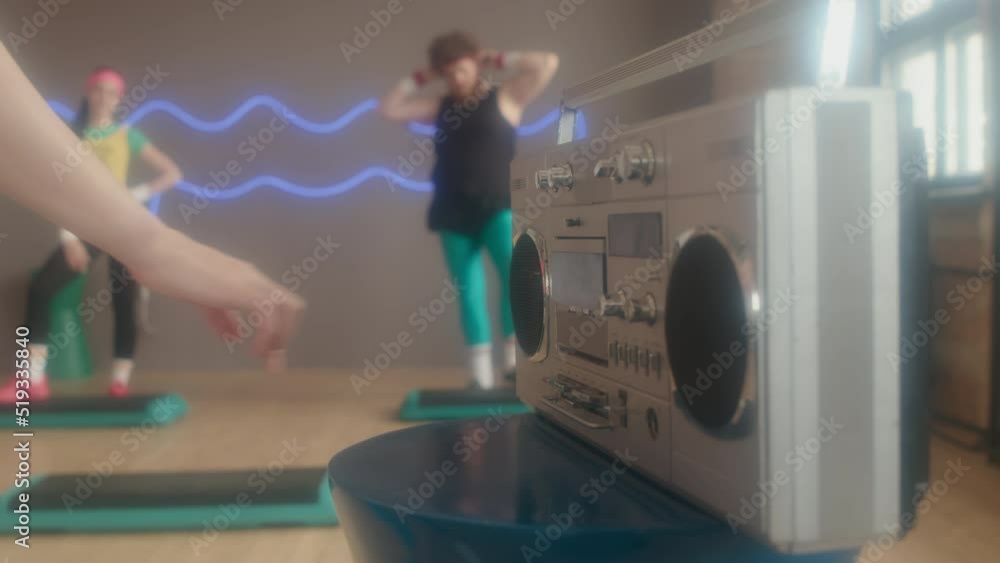 Locked-down of young blonde woman putting tape into retro stereo, starting group fitness lesson in 80s style