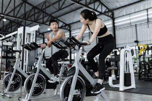 exercise concept The well-shaped lady and the muscular man being entertaining having small chat while riding the exercise bike machines