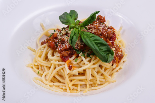 close-up spaghetti noodles topped with pieces of meat mixed with cheese and green vegetables served on a white plate