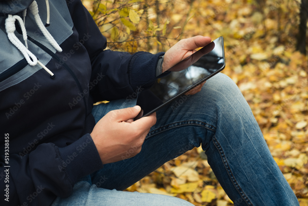 Man hipster using tablet in autumn forest during hiking trip. Travel concept, hike, fall season. Closeup Man hipster using tablet in autumn forest during hiking trip. Travel concept, hike, fall season. Closeup