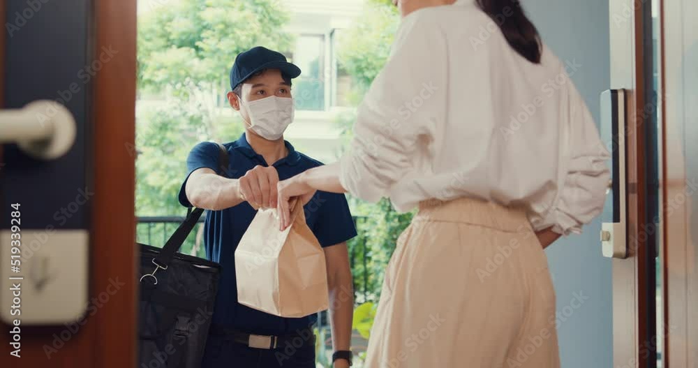 Young Asian delivery man wear mask in blue navy uniform carry case box knock door home online shopping paper bag to woman in front of door lady scan QR code payment on smartphone at house concept. Young Asian delivery man wear mask in blue navy uniform carry case box knock door home online shopping paper bag to woman in front of door lady scan QR code payment on smartphone at house concept.