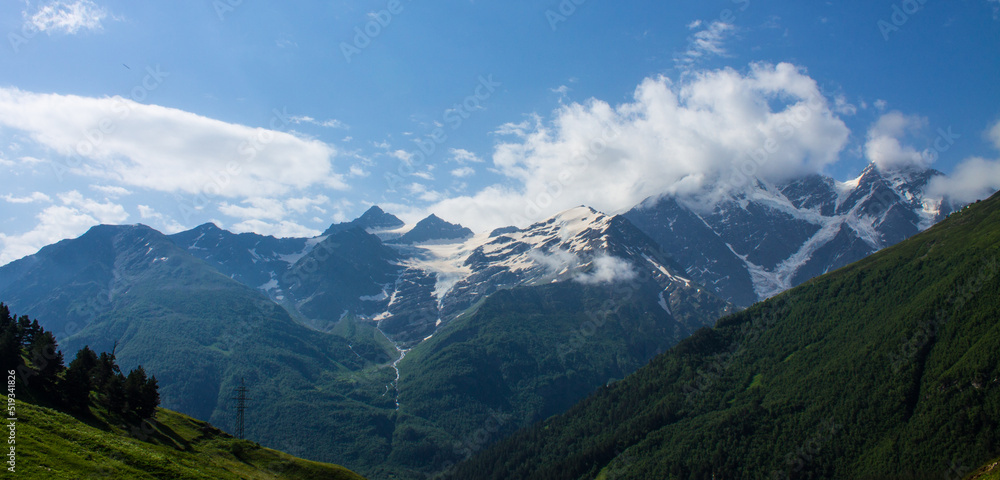 Silhouettes of high snow-capped peaks of the stone cliffs of the Caucasian ridge in the Elbrus region Russia on a clear sunny summer day and coniferous trees