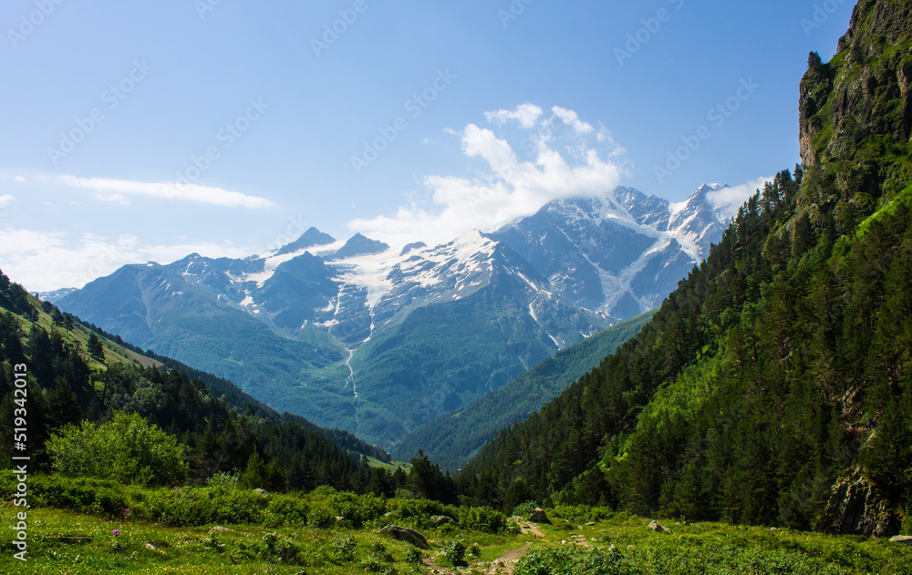 Pastoral landscape - green hillsides and high mountains with snowy peaks over a valley with alpine meadows on a clear sunny summer day in the Elbrus region in the North Caucasus in Russia
