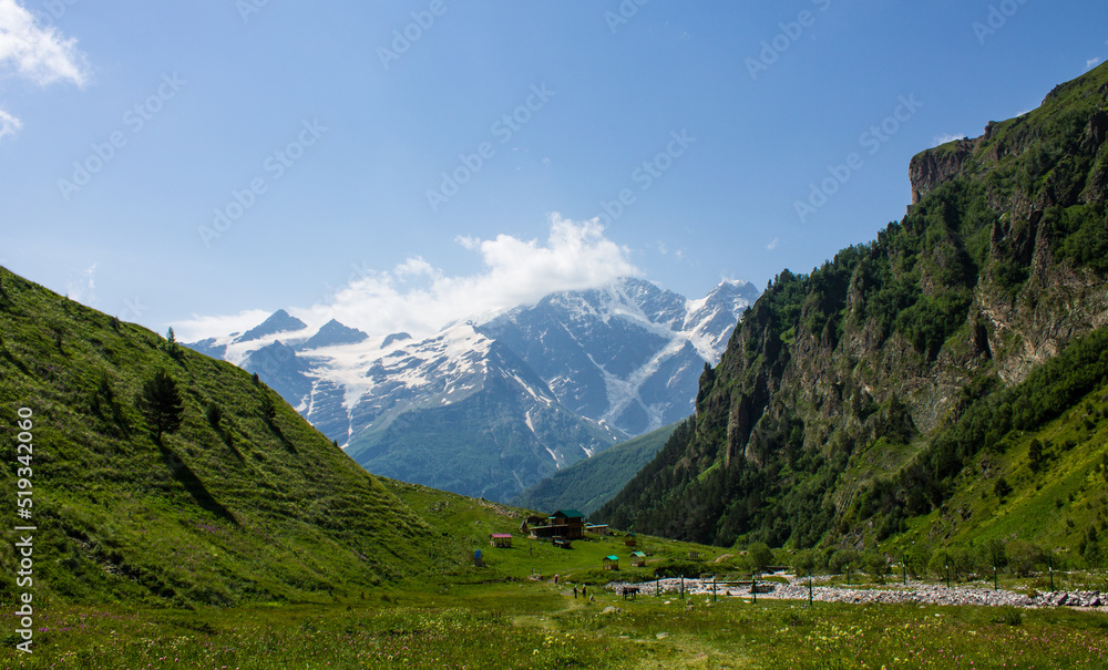 Beautiful landscape - green hills in the terskol valley with bright grass and high mountains with snow and peaks and glaciers on a clear summer sunny day in the elbrus region russia