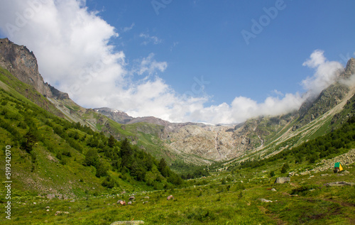 Fototapeta Naklejka Na Ścianę i Meble -  Mountain landscape with high stone cliffs and bright green grass on an alpine meadow in the Elbrus valley in the North Caucasus in Russia on a sunny summer day
