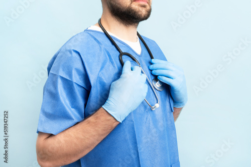 Portrait of smilin young and motivated doctor with stethoskope over neck and medical scrubs standing on the blue background. photo