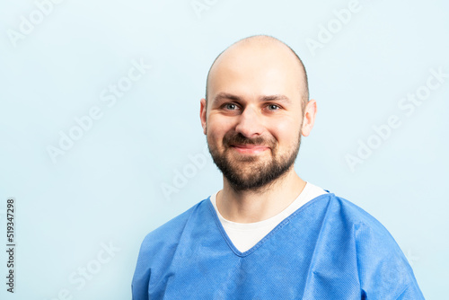 Portrait of smilin young and motivated doctor with stethoskope over neck and medical scrubs standing on the blue background.
