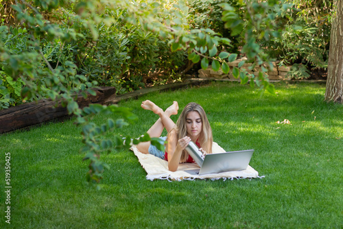 Top view of young woman lying in the garden working as a freelancer for her own online business