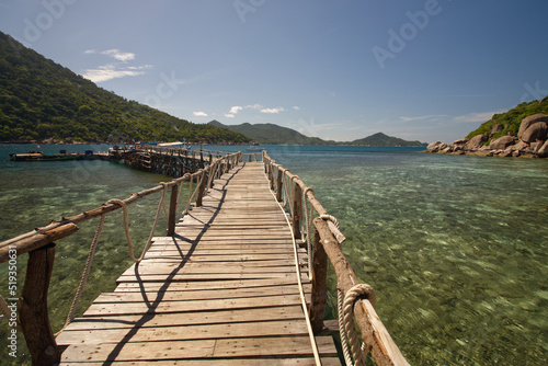 The scenery of wooden bridge to the port from south of Thailand.  The wooden bridge in the sea with blue sky and mountains. © Vimonrat