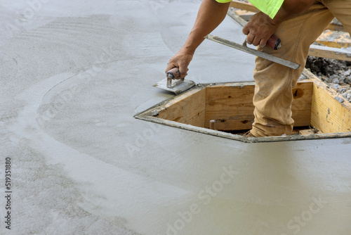 On the new cement floor, construction worker is using a stainless steel edger to form corner with the wet cement