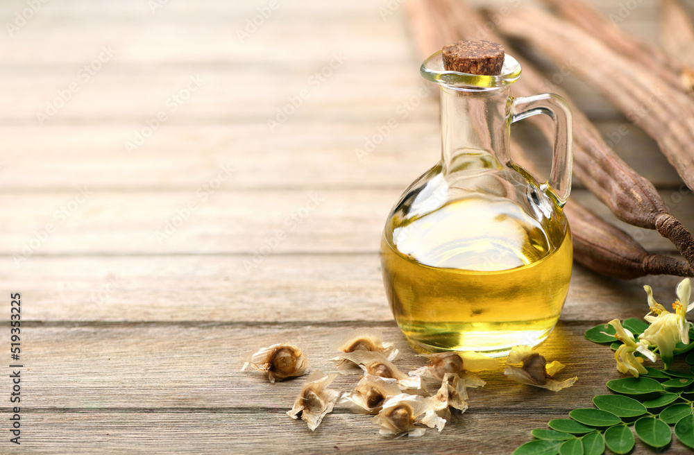 Moringa Oil in glass bottle with dried seeds and pods on wooden table Moringa Oil in glass bottle with dried seeds and pods on wooden table