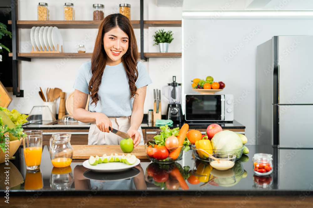 A happy young Asian woman looking at the camera preparing a healthy salad with vegetables on a cutting board in the home kitchen. Food cooking for couple husband and wife in a good relationship. A happy young Asian woman looking at the camera preparing a healthy salad with vegetables on a cutting board in the home kitchen. Food cooking for couple husband and wife in a good relationship.