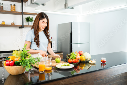 A happy young Asian woman preparing a healthy salad with vegetables on a cutting board on the home kitchen counter. Food cooking for couple husband and wife in a good relationship.