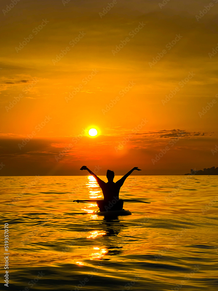 silhouette of a joyful happy girl hands up in the sea at sunset board sup