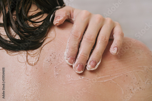 Faceless shot of woman using narutal scrub on her shoulder in the shower photo