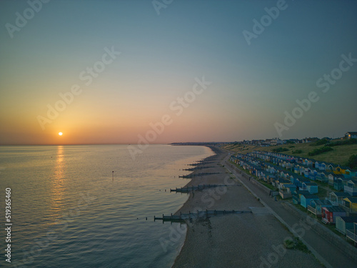 Sunrise over Whitstable beach with beach huts sun reflection in water red orange on watermelon sky