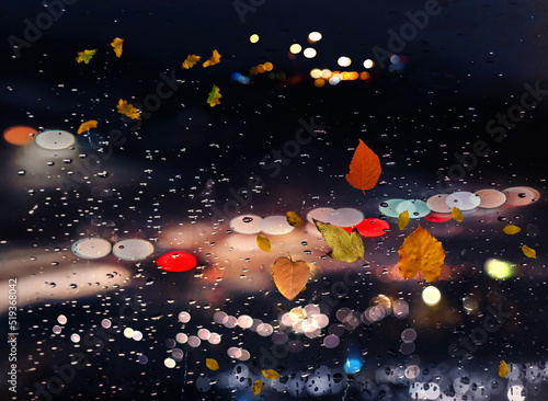 Fototapeta Naklejka Na Ścianę i Meble -  Autumn leaves on window rain drops and Autumn leaves fall night city traffic blurred light colorful reflection cold season background 