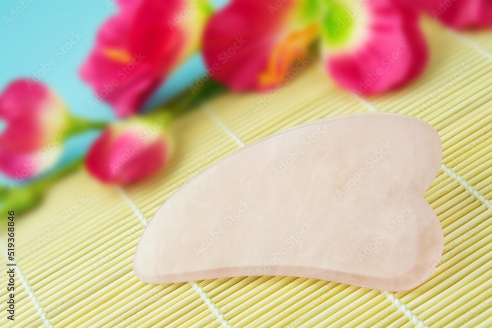Wellness and Beauty Massage Stone Gua-Sha and decoration with flowers closeup Wellness and Beauty Massage Stone Gua-Sha and decoration with flowers closeup