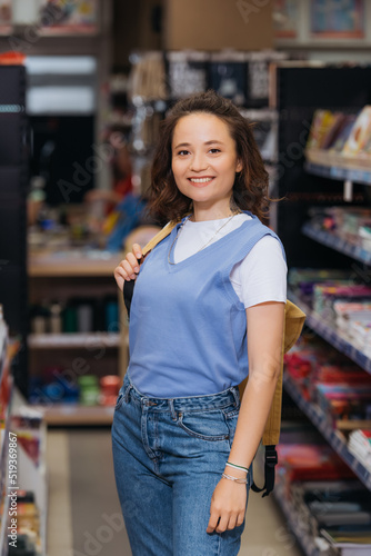 cheerful student with backpack looking at camera in stationery store.