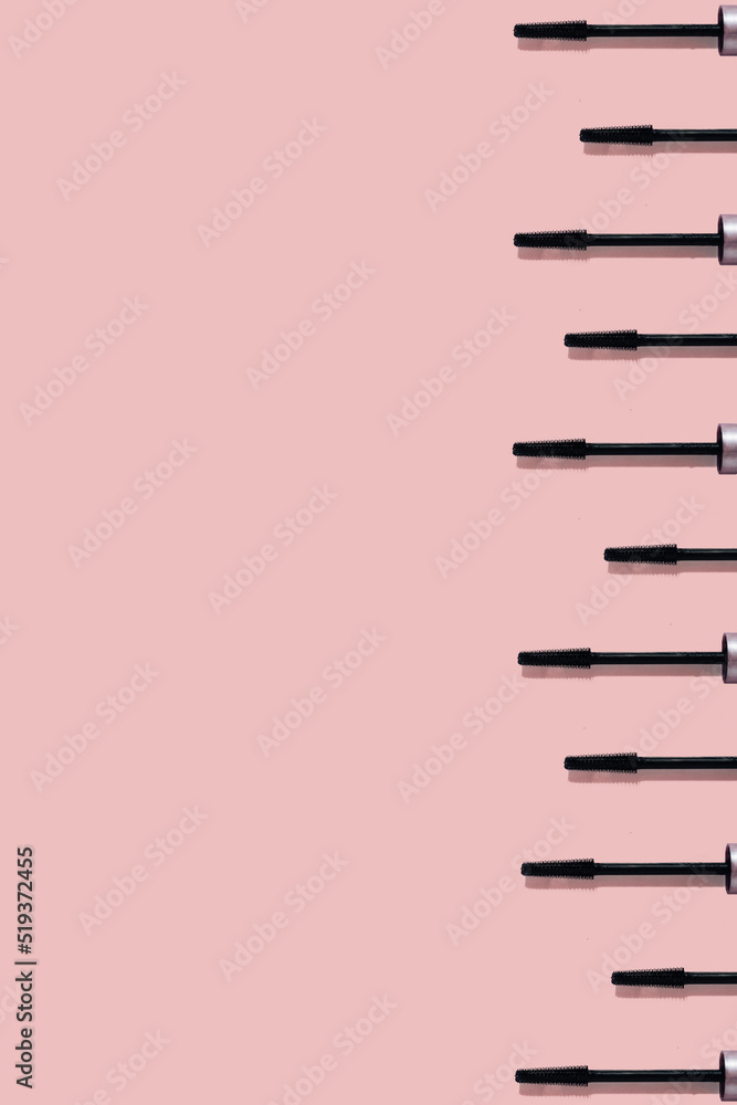 Set of many black mascara brushes with sharp shadows isolated on pink background with copy space. Beauty product smear pattern. .