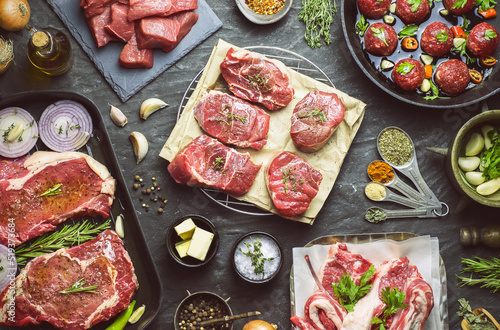 Different types of fresh raw meat sprinkled with seasonings and placed with organic ingredients on dark background. Top view with close-up.