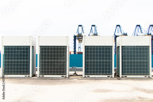 Big air conditioner compressor source heat pumps on wall outdoor on roof top of the building. It is used in large industrial buildings for cooling. with sky, container, auto remote crane background.