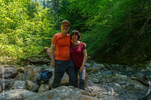 Ein Paar macht an einem heißen Sommertag ein Selfie in einem kühlen Bachbett. Ein Mann und eine Frau sitzen zwischen Felsen im Tal, Wanderer unterwegs im Schatten © Dieter
