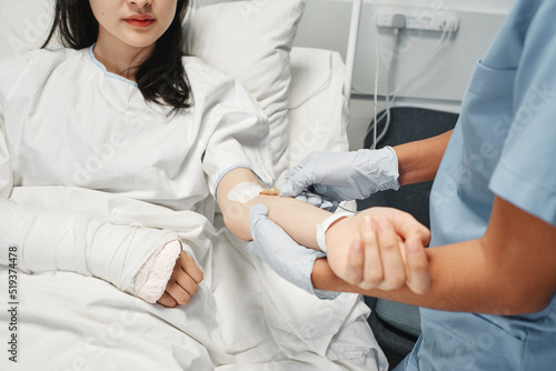 Horizontal shot of young Asian woman lying on hospital bed getting IV therapy in emergency room