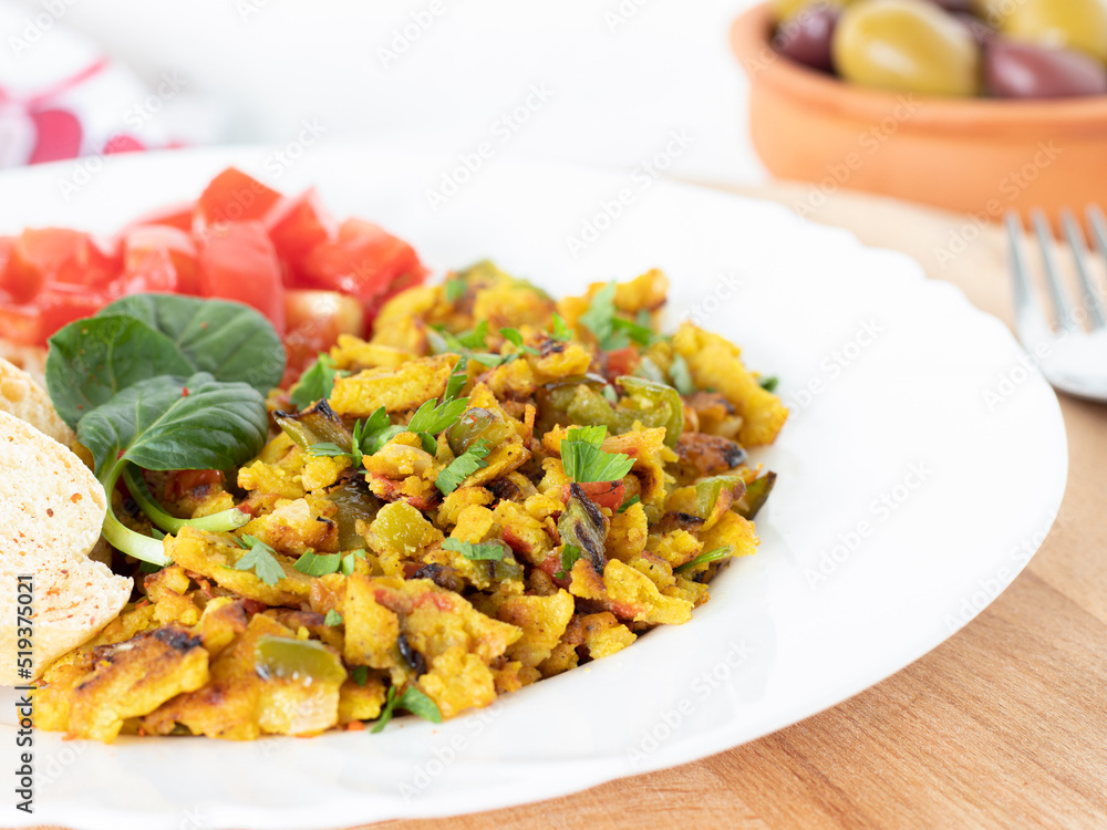 Vegan scrambled eggs with chickpea flour and fresh vegetables on a plate on a wooden table with white background. Egg-free omelet in a dish for breakfast or brunch. Healthy protein-rich meal. Closeup.