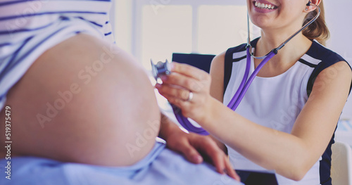 Young woman doctor with stethoscope and tablet speaking with pregnant woman at hospital.