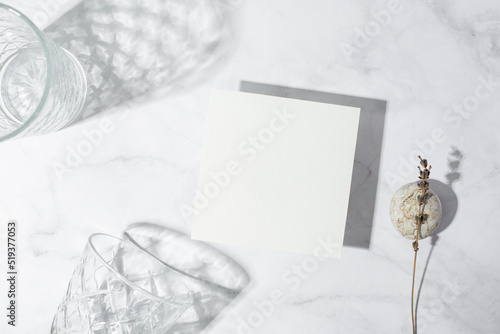 Still life scene with glasses on marble background in sunlight and blank business, greeting card, invitation mockup. Long harsh shadows. 