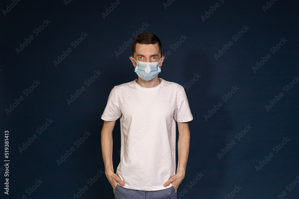 A man in a white T-shirt and protective mask stands against a blue background A man in a white T-shirt and protective mask stands against a blue background