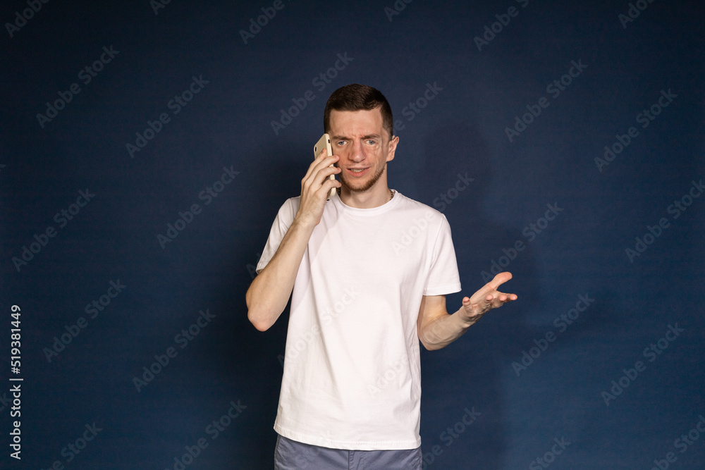 A man in a white T-shirt with Treacher Syndrome speaks on the phone