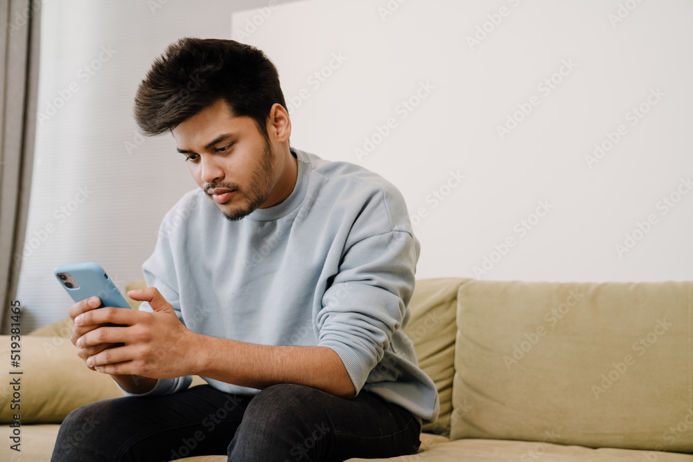 Young indian man sitting on sofa and scrolling social media Young indian man sitting on sofa and scrolling social media