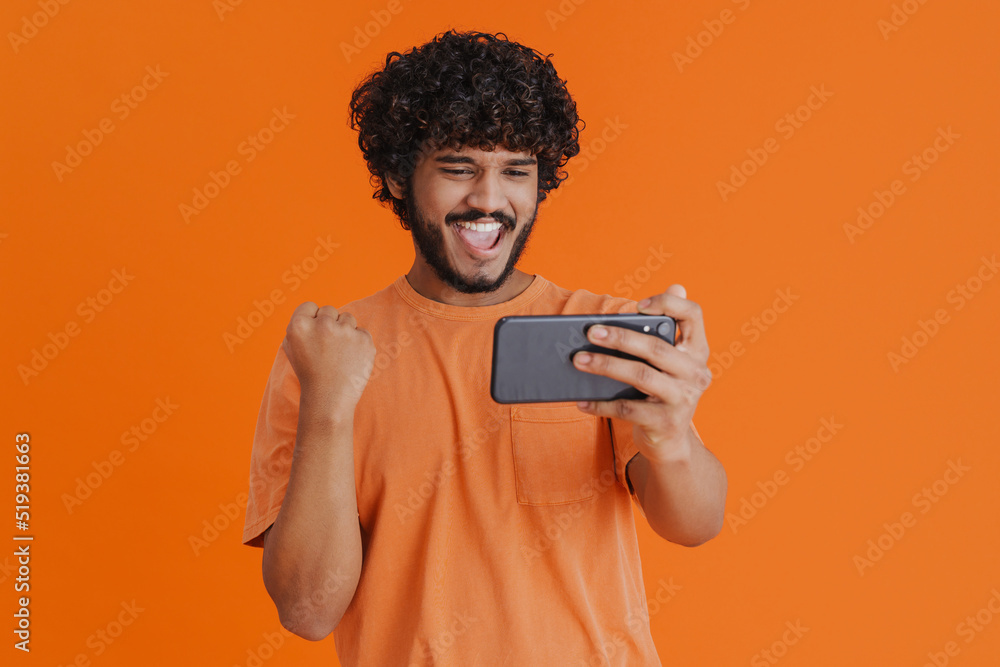 Portrait of young indian curly man holding phone celebrating victory Portrait of young indian curly man holding phone celebrating victory