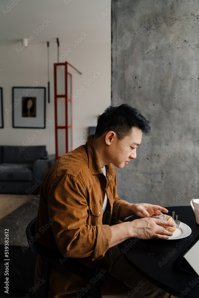 Asian man using tablet computer while having breakfast in kitchen
