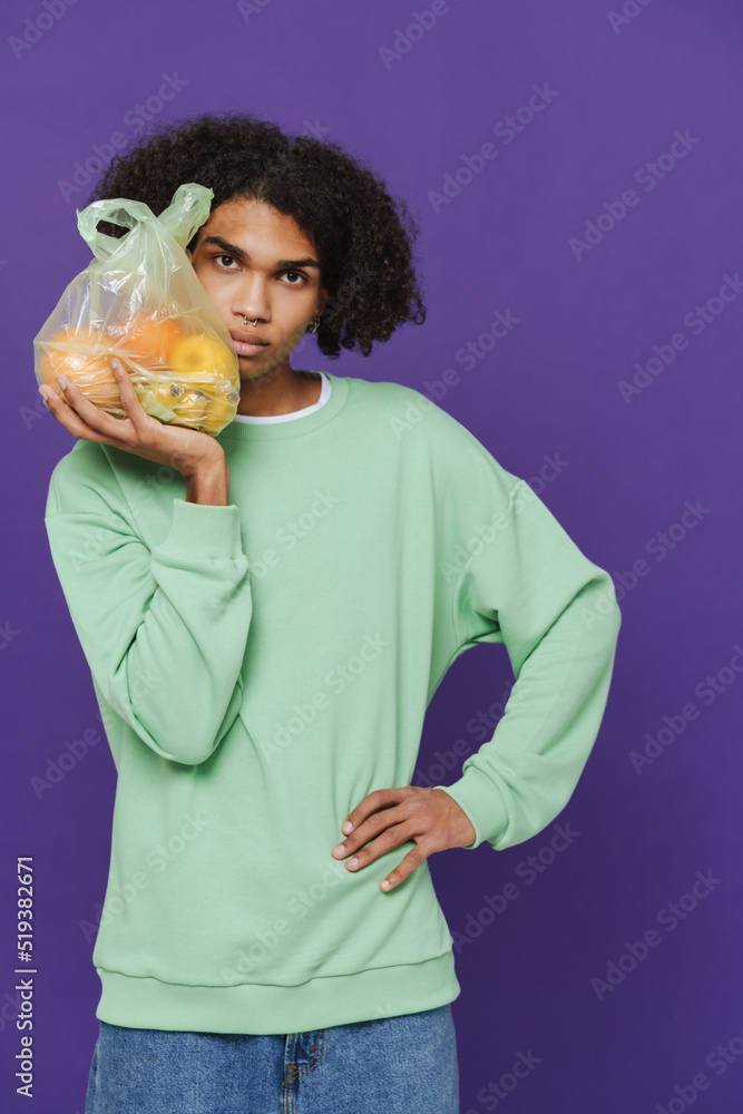 Young caribbean man holding and showing plastic bag with fruits Young caribbean man holding and showing plastic bag with fruits